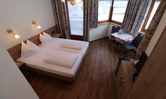 A cozy room with two single beds and wooden floor.  
Large windows provide plenty of daylight and there is a small table with chairs.