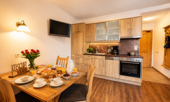 A modern kitchen with wooden cabinets and a dining table. 
On the table, breakfast ingredients and coffee are set.