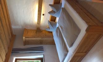A cozy bedroom with a large double bed and two pillows. The room has wooden paneling and a window with a view of the greenery.
