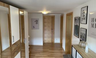 A bright hallway with wooden flooring and modern furniture. Various pictures hang on the walls and there is a large mirror.