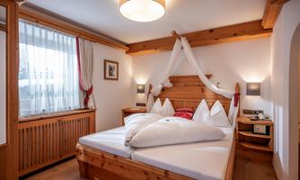 A cozy bedroom with a large bed and wooden furniture. The room is bright and cheerful, with a window and decorative curtains.
