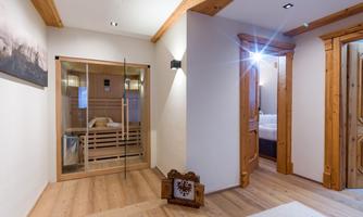 A modern hallway with wooden details and a glass sauna room. There are bright walls, warm lighting, and a cozy carpet.