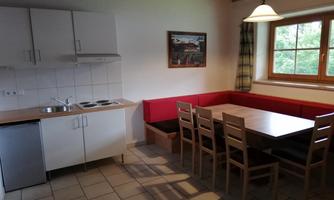 A bright kitchen with a dining table and chairs. In the background, there is a window overlooking nature.