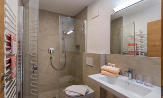 A modern bathroom with a glass shower and a white sink. The walls are painted in neutral colors, and towels are neatly arranged.