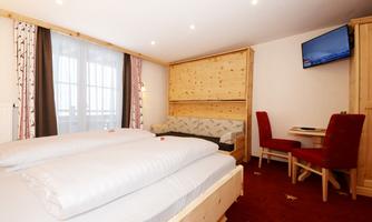 A comfortable room with two beds, a sofa, and a table. Large windows provide plenty of natural light.
