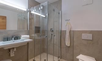 A modern bathroom with a glass shower and an elegant, bright color scheme. The amenities include a sink, towels, and a toilet.