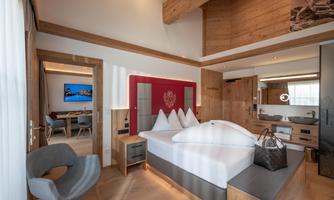 A modern hotel room with wooden elements and a large bed. The room is bright and features a television as well as a seating area.