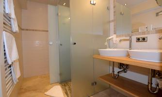 A modern bathroom with a glass shower and two sinks. Clean towels hang on the wall, and the floor is made of light material.