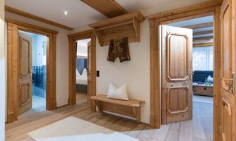 A cozy hallway with wooden details and two doors. A bench and a traditional garment are visible.