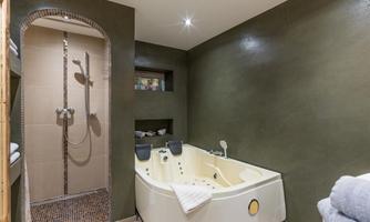 A modern bathroom with a bright bathtub and a rain shower. The walls are painted in an elegant gray tone and there is a towel on the floor.