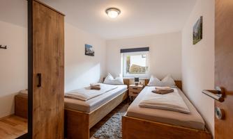 A cozy room with two single beds and wooden interior. The window offers a view outside and the room is brightly lit.
