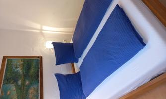 A simple bedroom with a bed that has two blue blankets and pillows. A picture hangs on the wall, and there is a small lamp.