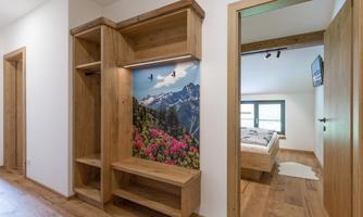 A modern hallway with wooden shelves and a beautiful mountain landscape on the wall. Two doors lead to bedrooms with a cozy atmosphere.