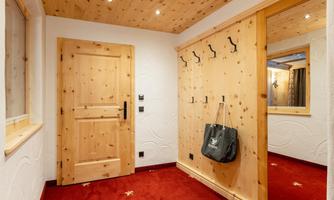 A cozy entrance area with wooden paneling and a red carpet. Several coat hooks are hanging on the wall and there is a mirror.