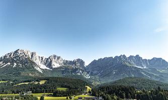 An impressive mountain landscape with high peaks and a clear sky. The green meadow in the foreground complements the picturesque panorama.