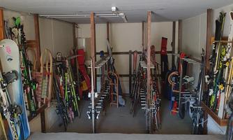 A well-organized storage room with many skis, snowboards, and bicycles. The equipment is neatly stored on shelves.