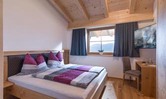 A cozy bedroom with a double bed and colorful cushions. The room has wood paneling and a window overlooking the landscape.