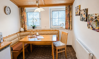 A cozy dining area with a wooden table and a bench. The walls are adorned with pictures and there is plenty of natural light coming through the windows.