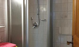 A small bathroom with a shower and a toilet. Colorful towels are placed on a shelf.