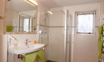A modern bathroom with a shower and a sink. The walls are light, and there is green decoration with towels.