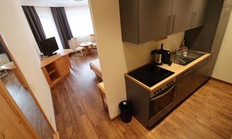 A modern kitchen with a cooktop and wooden cabinets. In the background, a cozy living area is visible.
