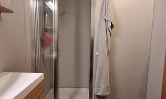 A modern bathroom with a shower and a wooden sink. A towel hangs on the wall and the floor is tiled with dark tiles.