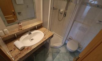 A bathroom with a sink, a mirror, and a shower cabin. The walls are tiled and the floor has a light color.