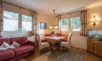 A cozy living kitchen with a red sofa and a dining table. Large windows provide plenty of daylight and a view outside.