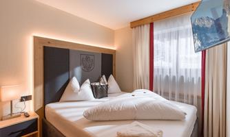 A cozy bedroom with a large bed and modern furniture. The room has bright walls and a window with curtains.