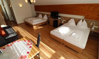 A cozy room with two beds and a sofa corner. There is a table with a tablecloth and a warm wooden floor.