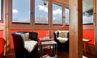 A cozy room with two black armchairs and a small table. Through large windows, there is a view of the mountains and the blue sky.