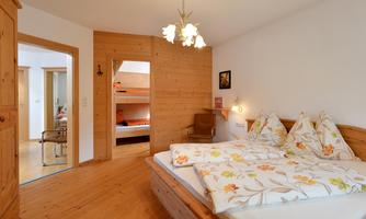 A cozy bedroom with wooden walls and a large bed. In the background, additional sleeping options are visible.