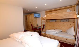 A cozy room with a double bed and a bunk bed. There is a television and a table with chairs.