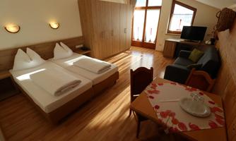 A cozy room with two beds, a table, and a living area. Large windows provide plenty of daylight.