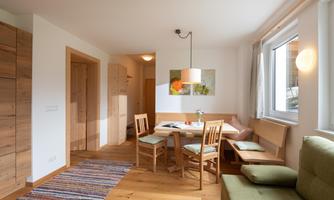 A cozy living space with a dining area and wooden floor. The walls are light and the window lets in plenty of natural light.