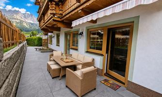 A cozy terrace with seating and a table. In the background, mountains and a clear sky can be seen.