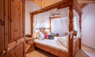 A cozy bedroom with a four-poster wooden bed. The warm wood fittings and the white curtains create an inviting atmosphere.