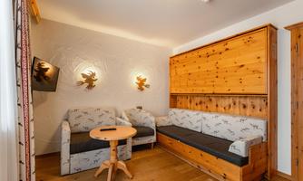 A cozy living space with a wooden bench and a round table. A TV and decorative lamps are hanging on the wall.