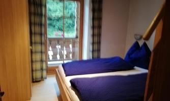 A cozy bedroom with two separate beds and blue bedspreads. The window offers a view of a green outdoor area.
