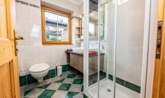 A modern bathroom with a shower, toilet, and a sink. The walls are tiled and there is a window that provides natural light.