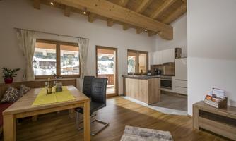 A cozy living room with a wooden table and modern furniture. Large windows let in plenty of light and offer a view outside.