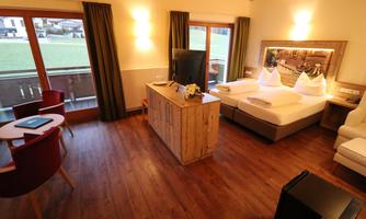 A cozy room with wooden floor and modern design. The furnishings include a bed, a television, and a small table with chairs.