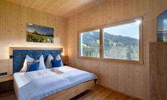 A cozy bedroom with wooden paneling and a view of the mountains. The room is bright and invites you to relax.