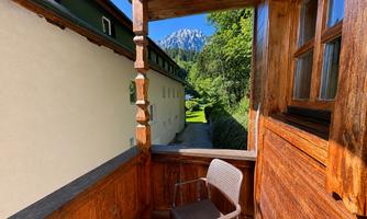 A balcony with wooden cladding and a chair. In the background, mountains and trees are visible.
