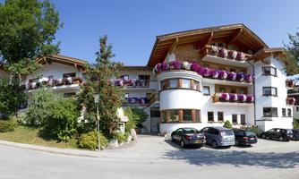 A picturesque hotel with balconies adorned with colorful flowers. Surrounded by trees and a clear blue sky.