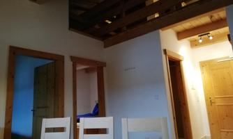 A bright interior with a wooden ceiling and several doors. A table is surrounded by white chairs that create a cozy impression.