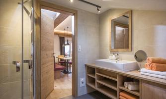 A modern bathroom with bright tiles and wooden details. The sink is well-equipped and there are several towels in orange.