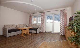 A cozy living room with a couch, a table, and a television. Through the windows, there is a view of a snowy landscape.