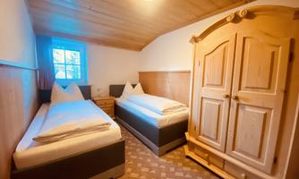 A cozy bedroom with two single beds and a wooden wardrobe. Large windows ensure plenty of light and an inviting atmosphere.