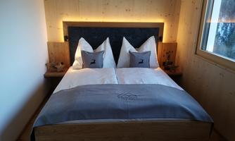 A cozy bedroom with a large bed and two pillows. The walls are made of light wood, and the room has large windows for plenty of daylight.